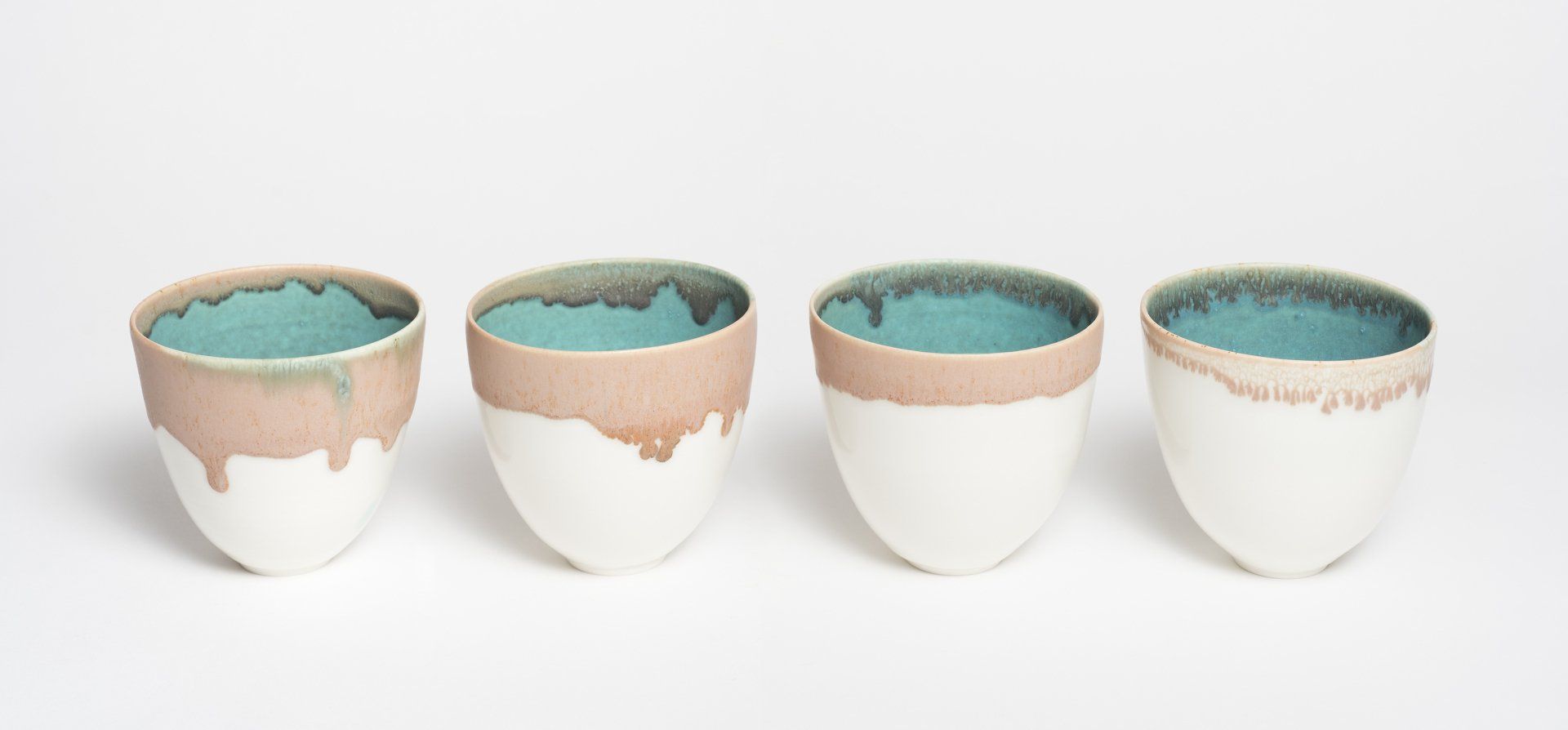 A row of four white cups with a blue rim on a white surface.
