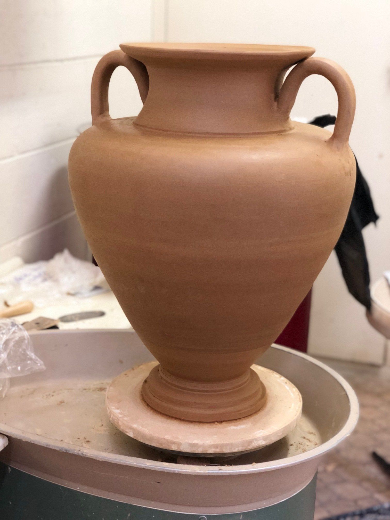 A large clay vase is sitting on a pottery wheel