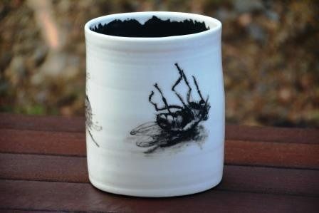 A white cup with a picture of a fly on it