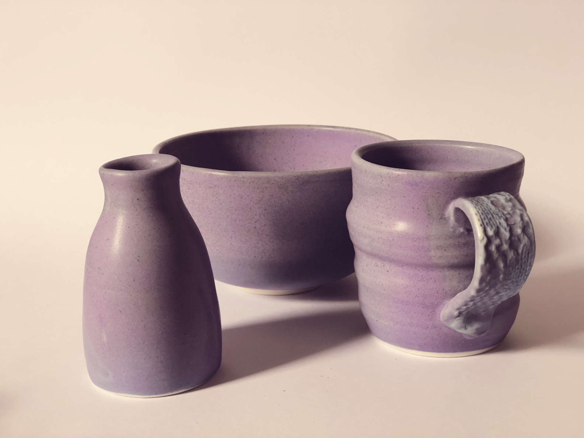 A purple vase a bowl and a mug are on a table