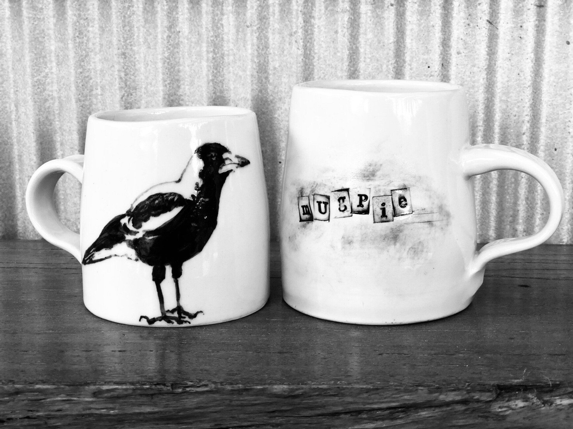 A black and white photo of two coffee mugs with a bird on them.
