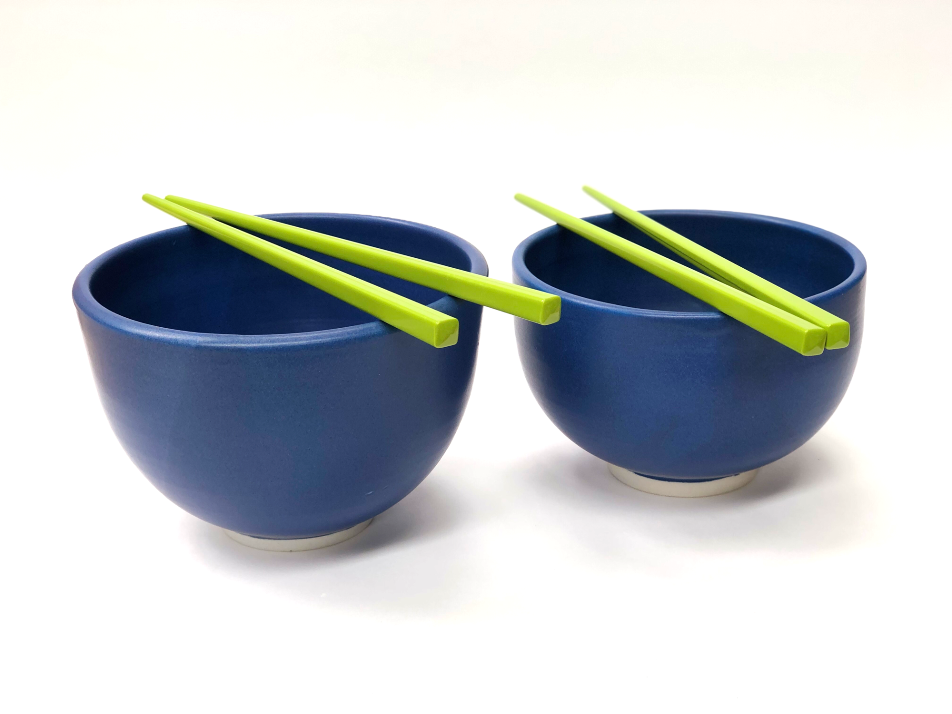 Two blue bowls with green chopsticks in them