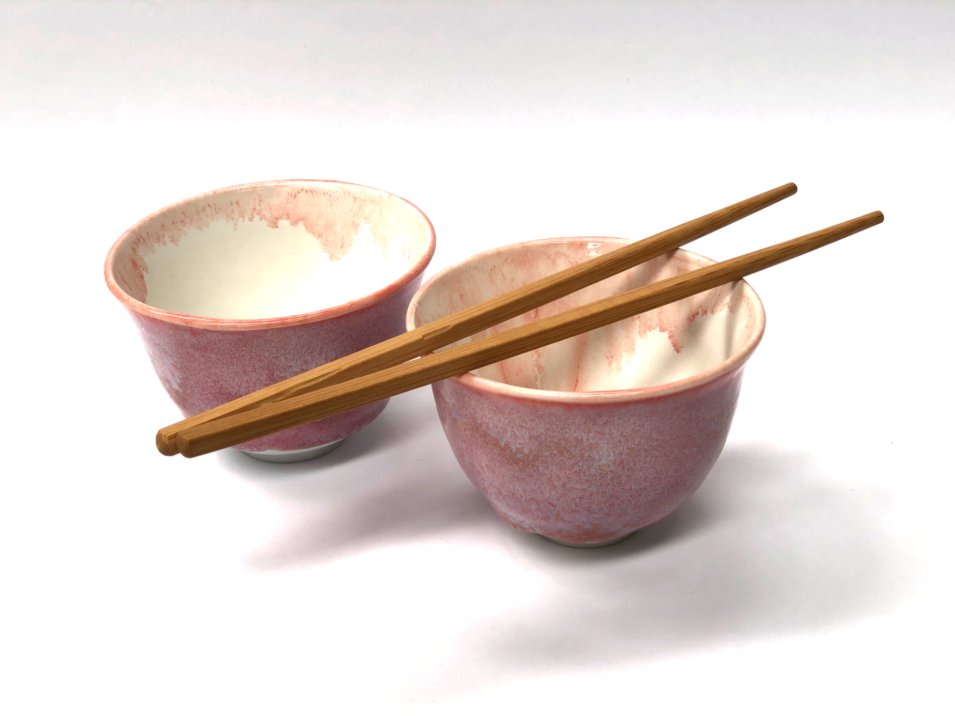 Two pink bowls with chopsticks in them on a white surface
