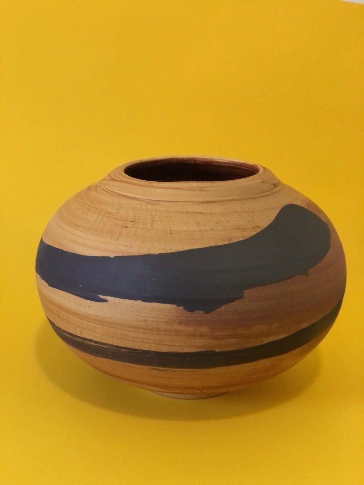 A brown and black vase is sitting on a yellow surface