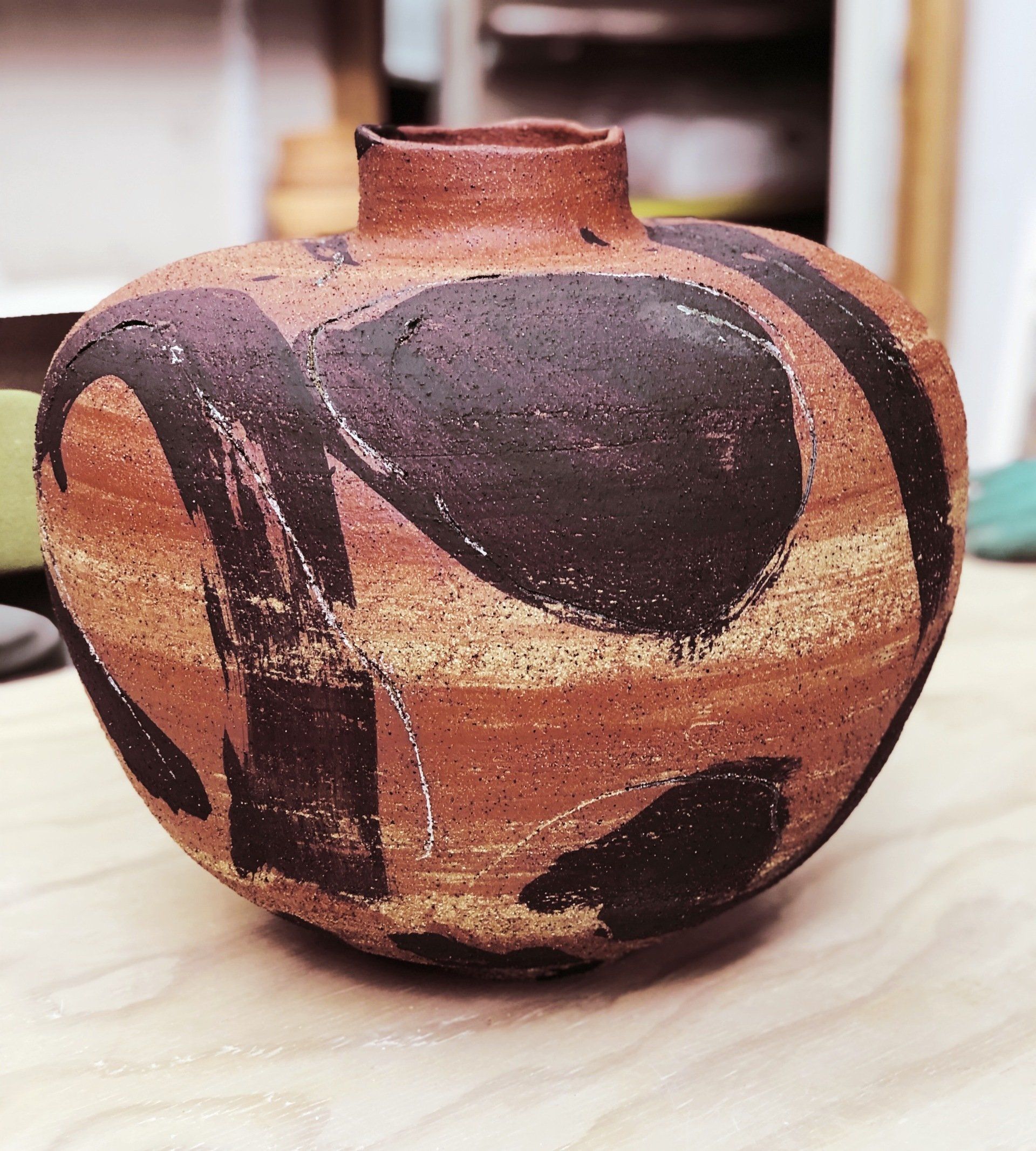 A brown and black vase is sitting on a wooden table