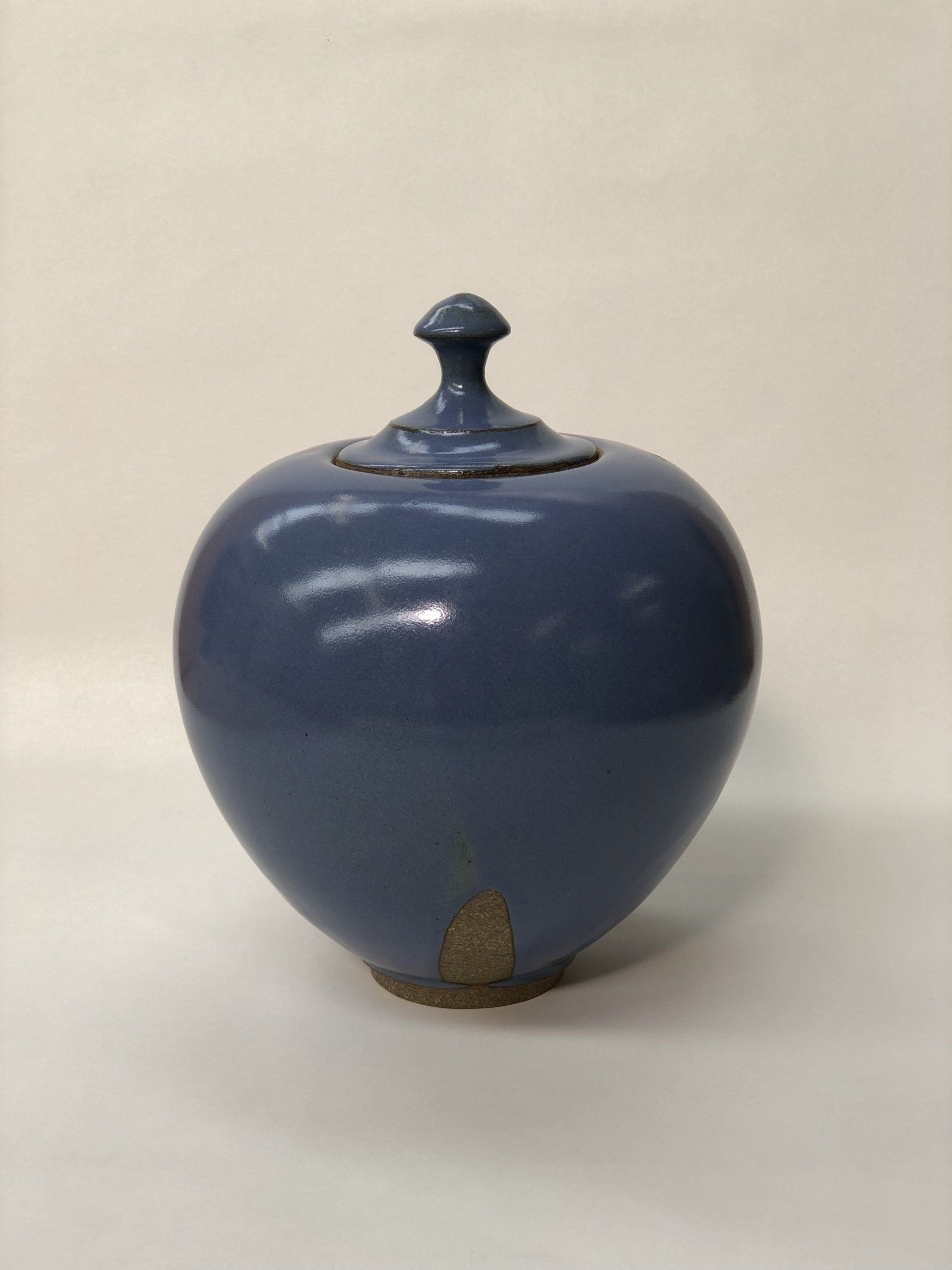 A blue vase with a lid is sitting on a white surface.