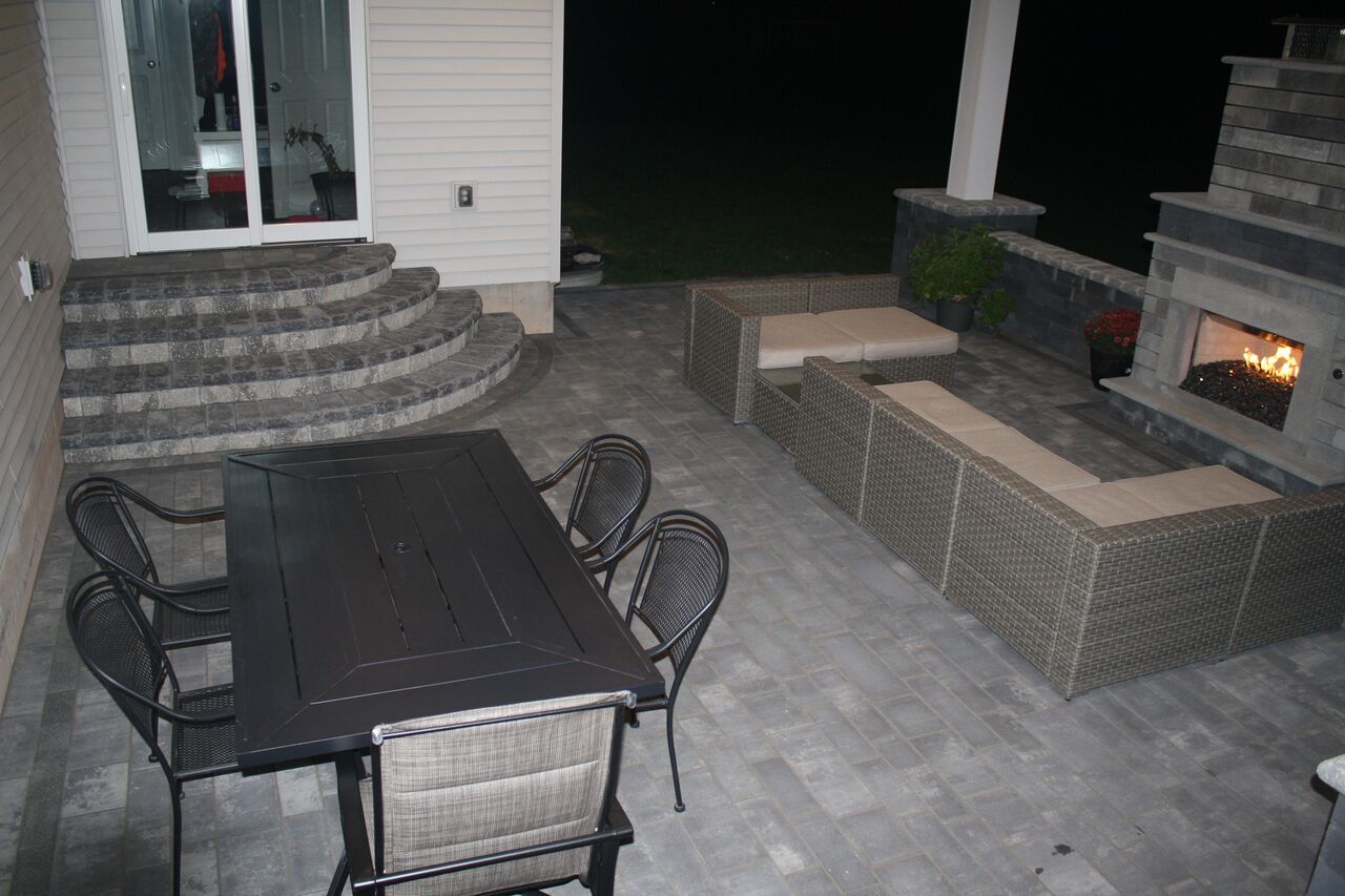 a patio with a table and chairs and a fireplace at night .