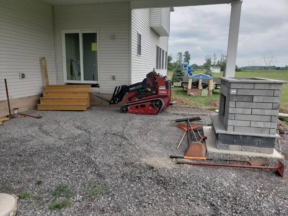 a tractor is parked on the gravel in front of a house .