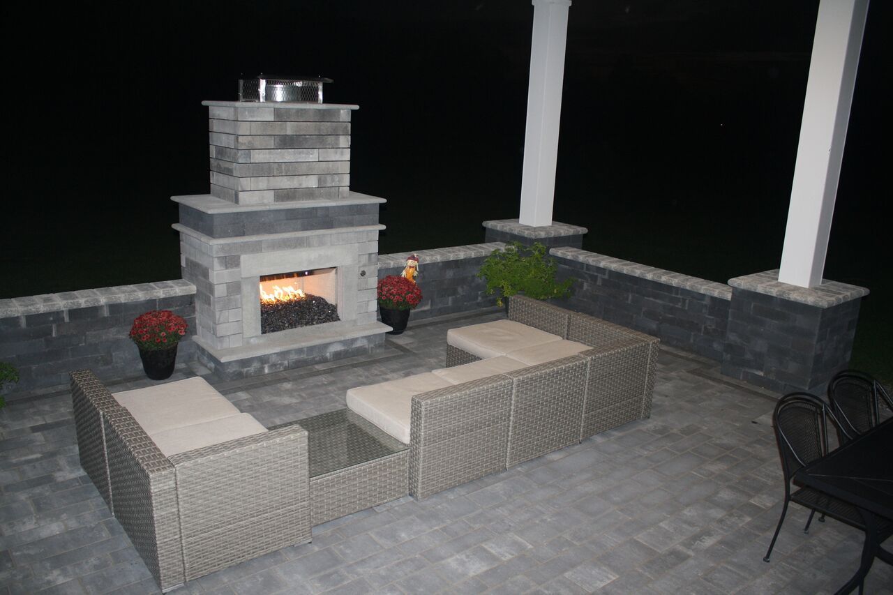 a patio with a fireplace and wicker furniture at night .