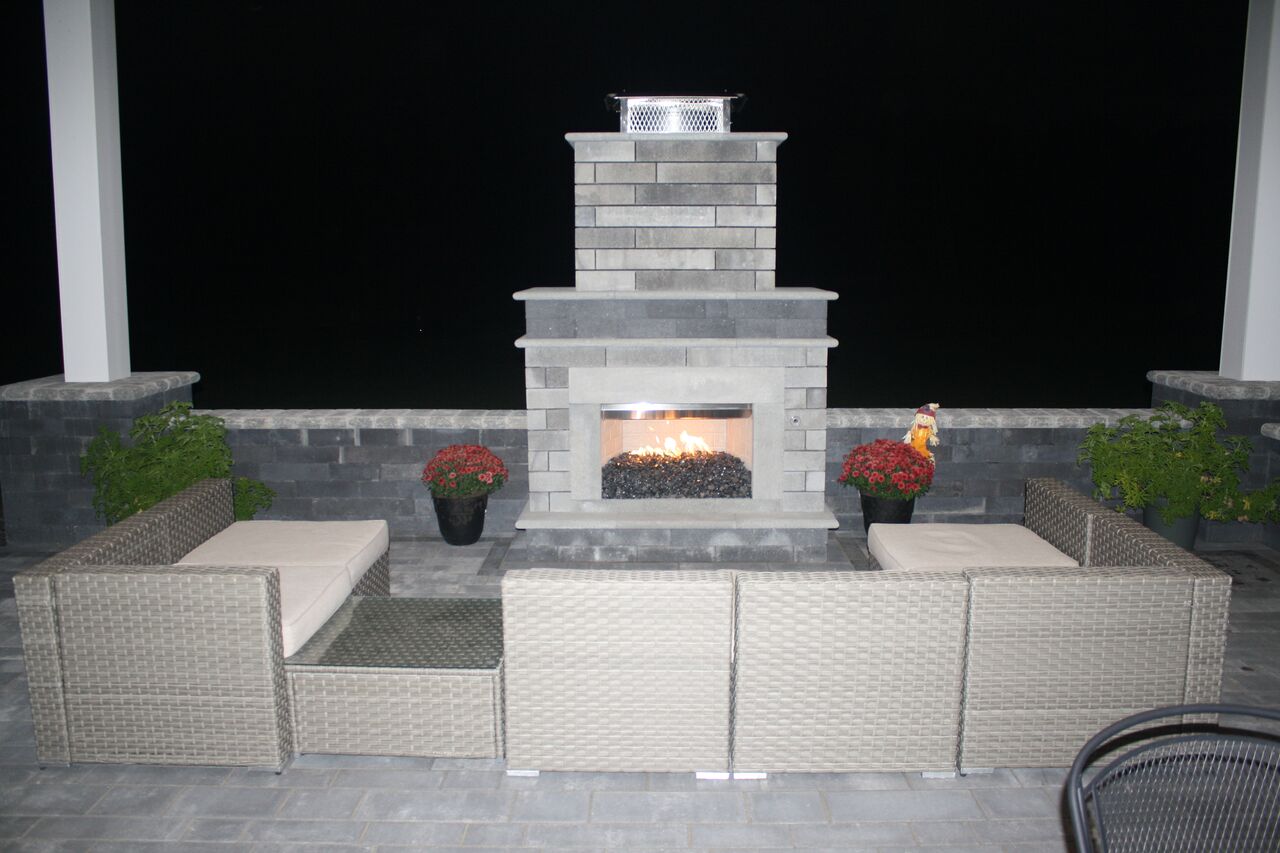 a patio with a fireplace and a couch and chairs at night .