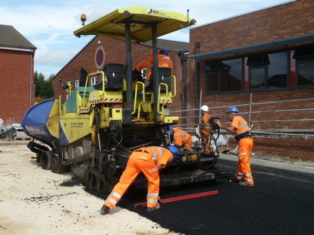 Workers spreading asphalt behind a large machine