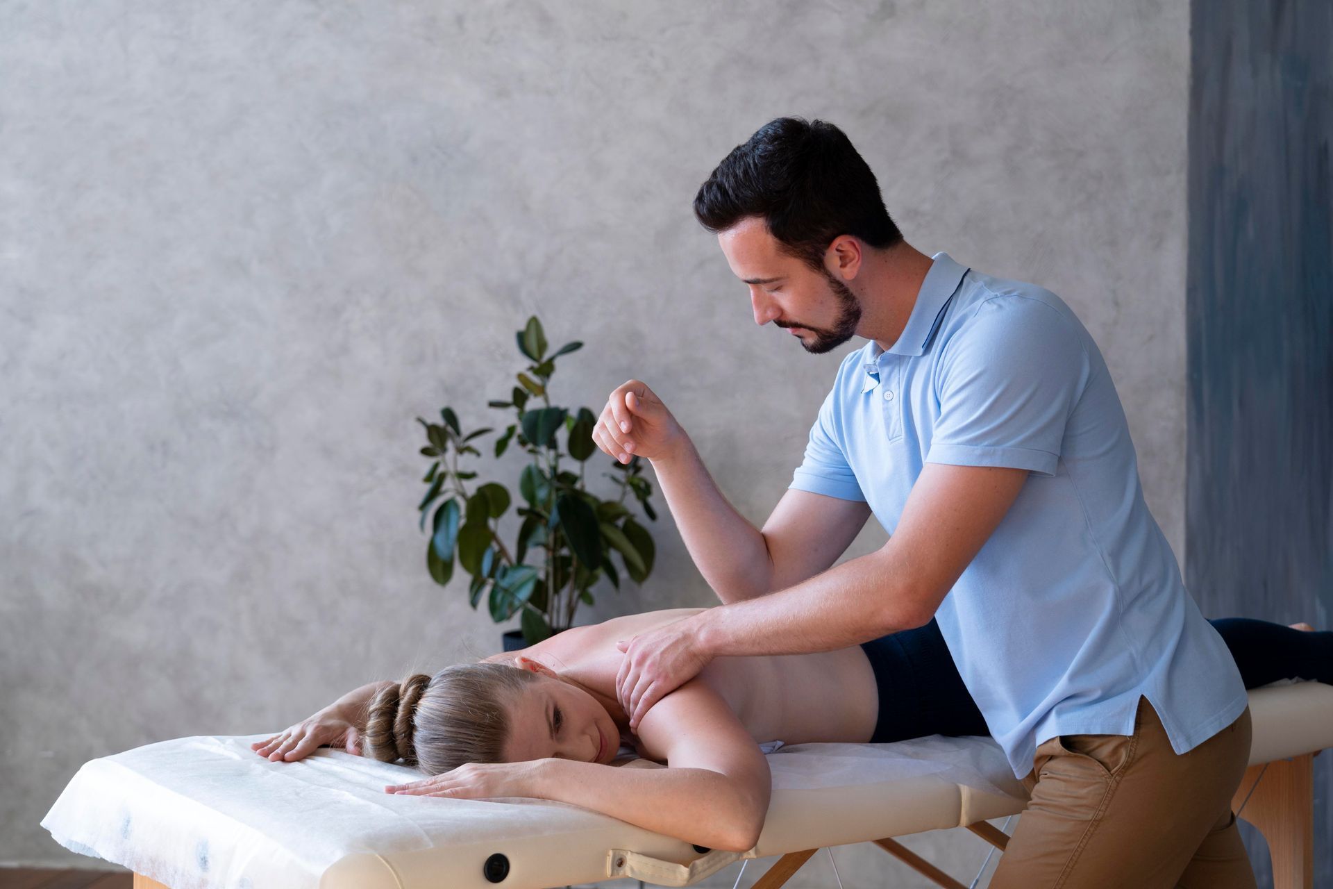 Therapist using elbow to massage client's back on a massage table indoors.