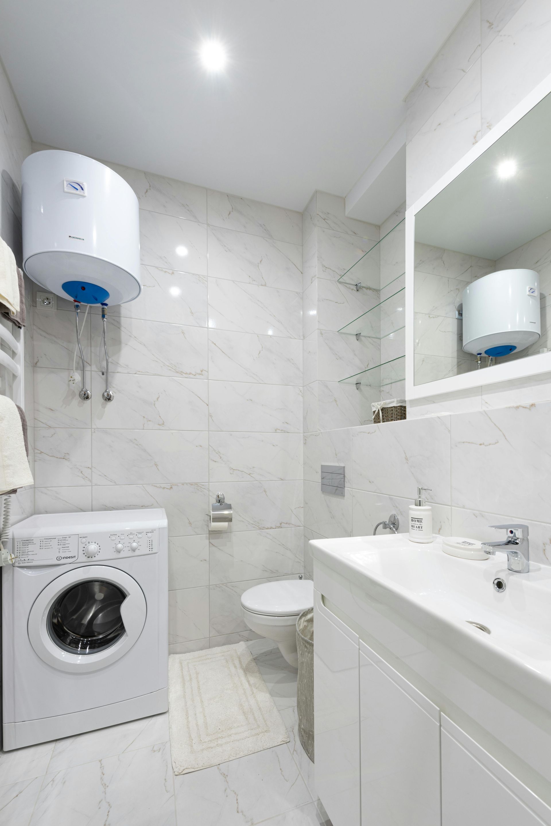 Compact bathroom with washing machine, sink, toilet, mirror cabinet, and wall-mounted water heater.