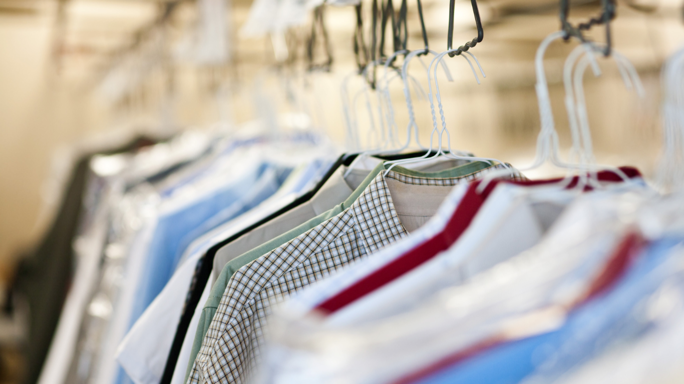 A row of shirts hanging on metal hangers in a closet.