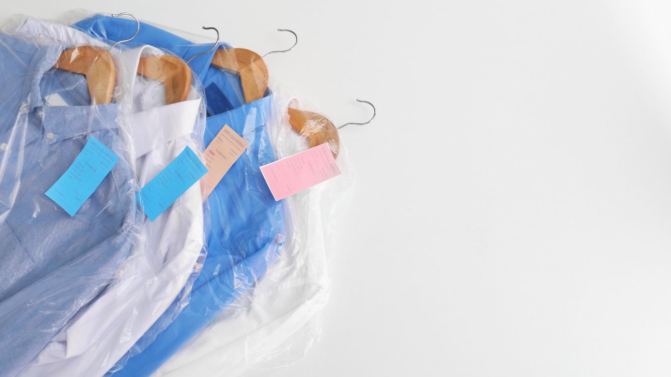 Four shirts wrapped in plastic and hung on wooden hangers against a white background, each with a colored tag.