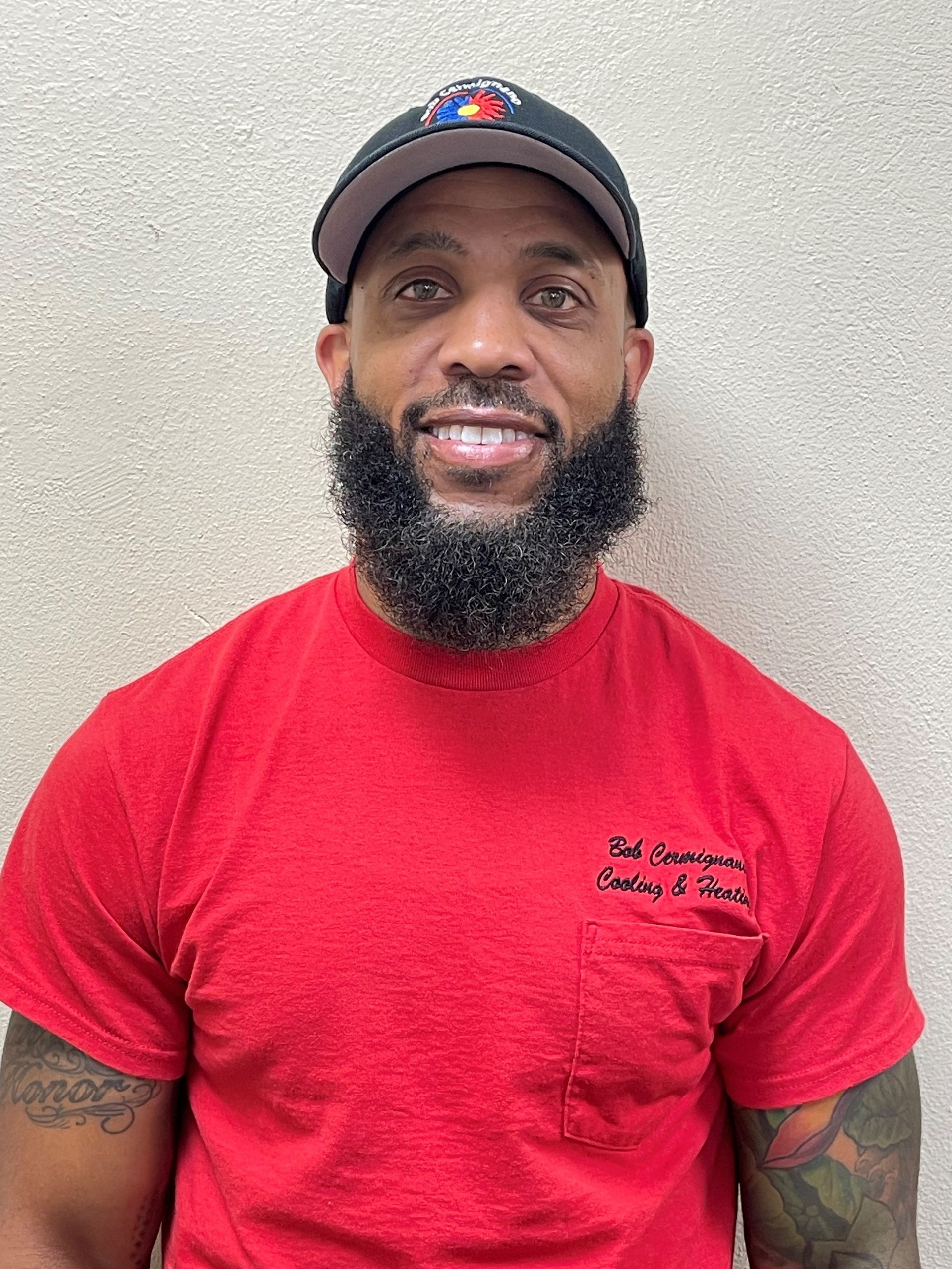 A man with a beard is wearing a red t-shirt and a black hat.