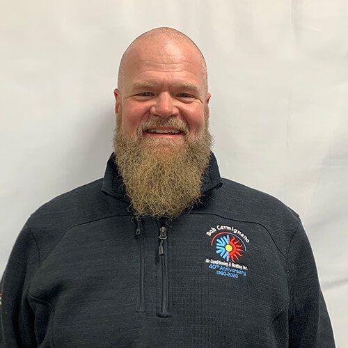 A man with a beard is wearing a black jacket and smiling.