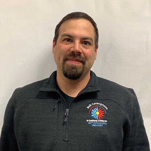 A man with a beard is wearing a black jacket and smiling for the camera.