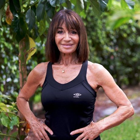 A woman in a black tank top is standing in front of a tree.