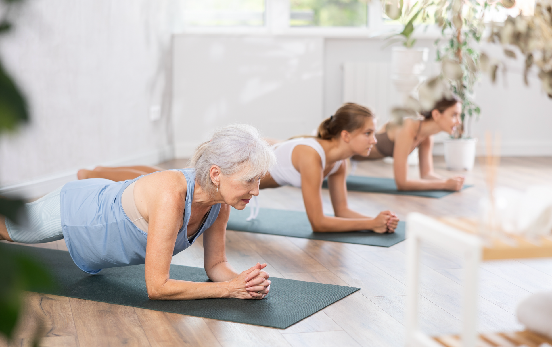 Three women are doing plank exercises on yoga mats in a gym.