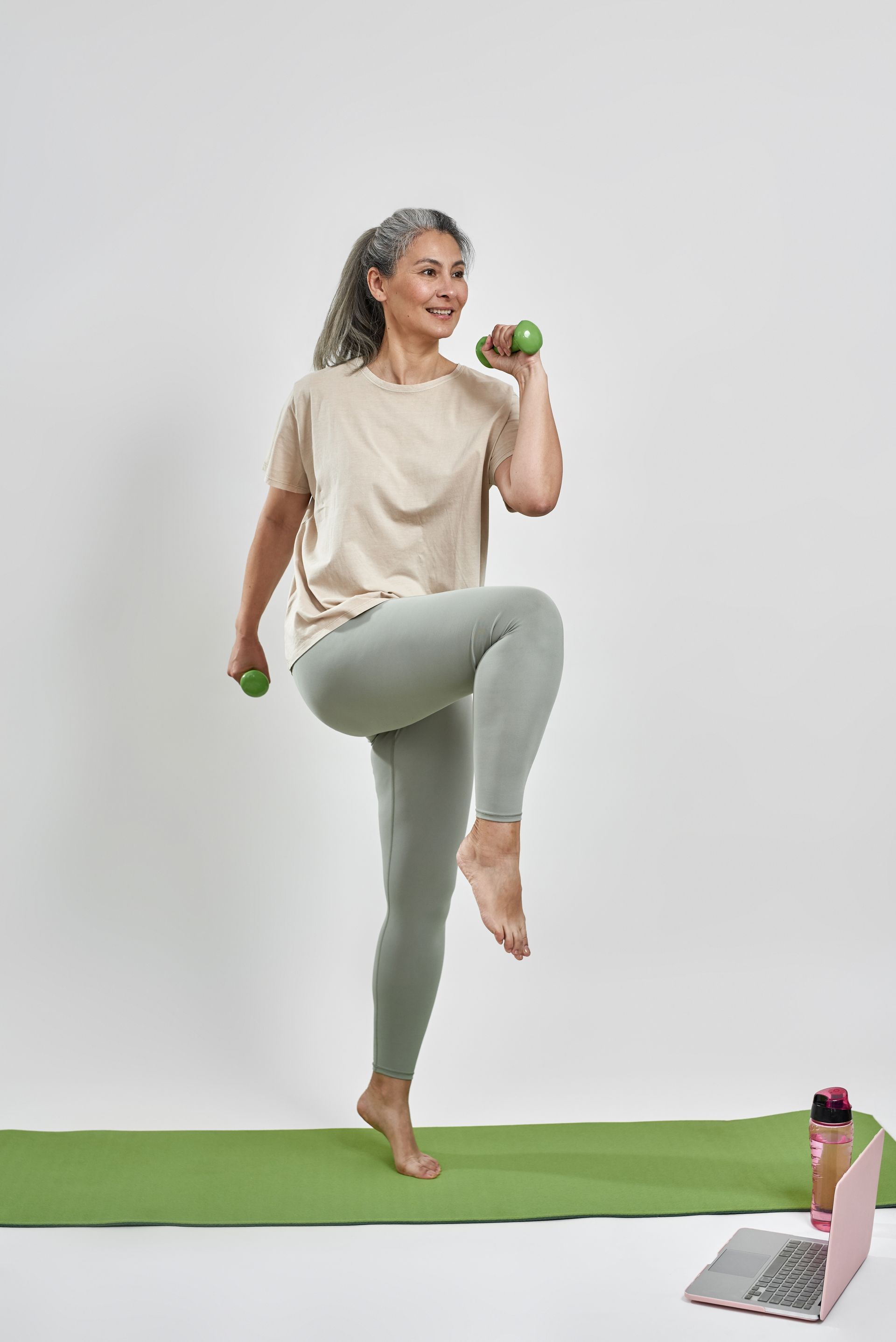 A woman is doing exercises on a yoga mat while holding dumbbells.