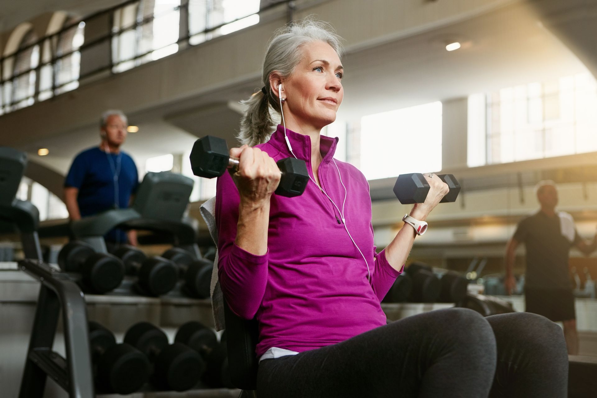 An older woman is lifting dumbbells in a gym.