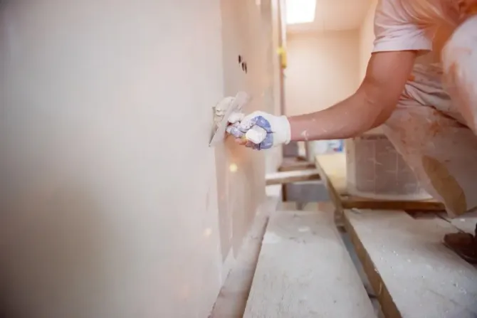 Worker applying plaster mud to a drywall corner joint.
