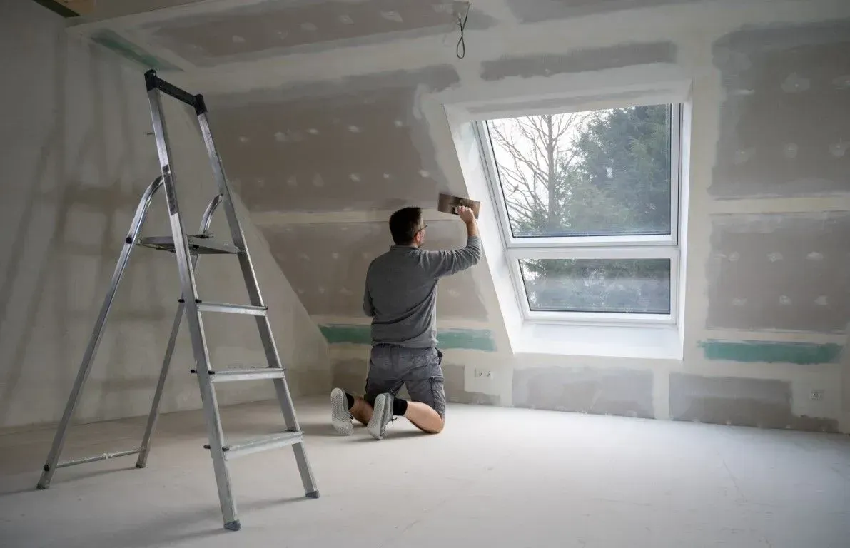 Worker applying joint compound near an attic skylight