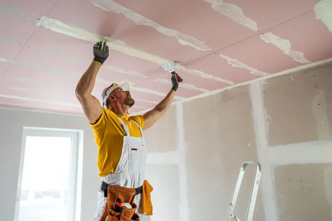 Drywall contractor taping and mudding a ceiling seam.