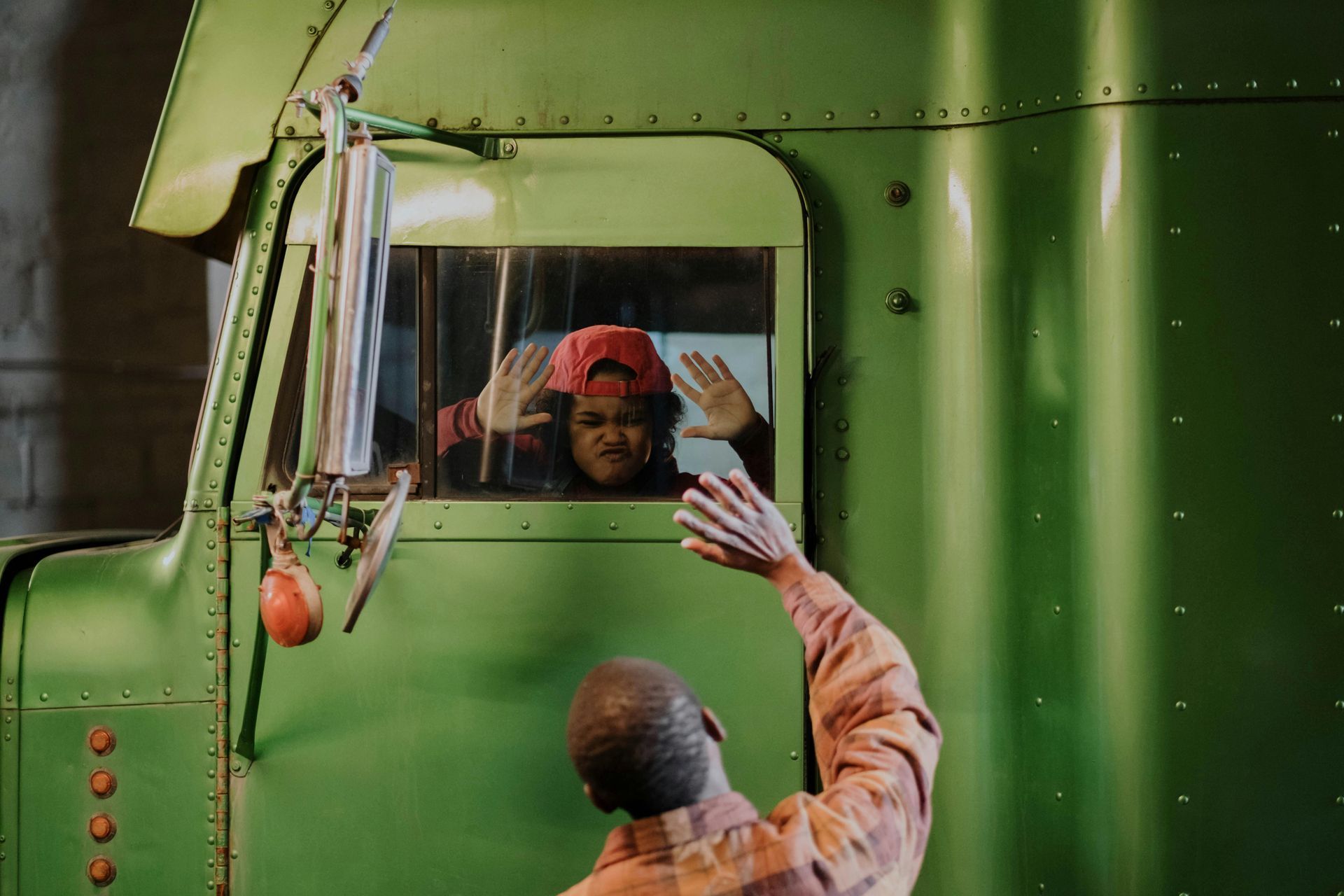 A man is waving from the window of a green semi truck.