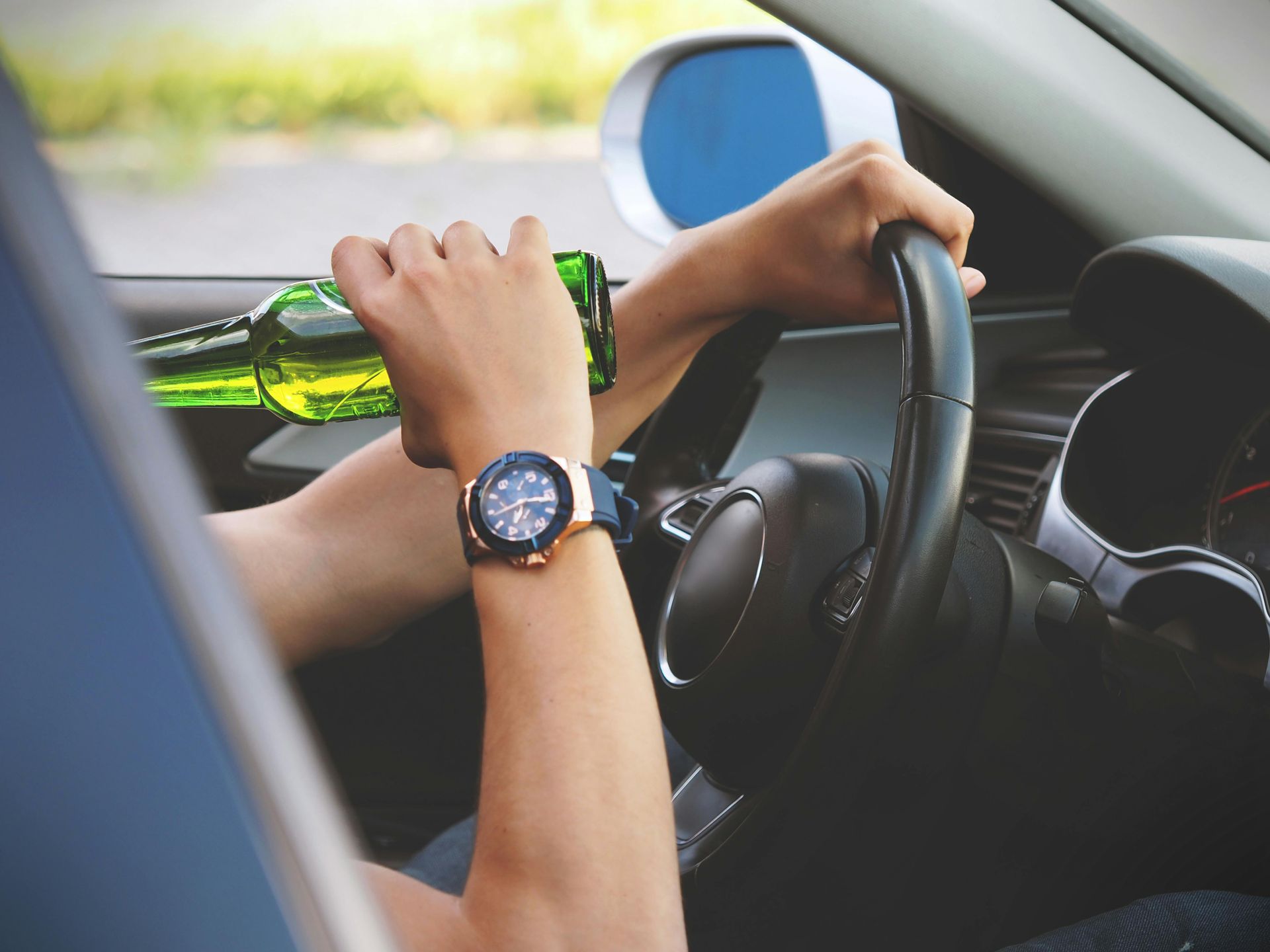 A person is holding a bottle of beer while driving a car.