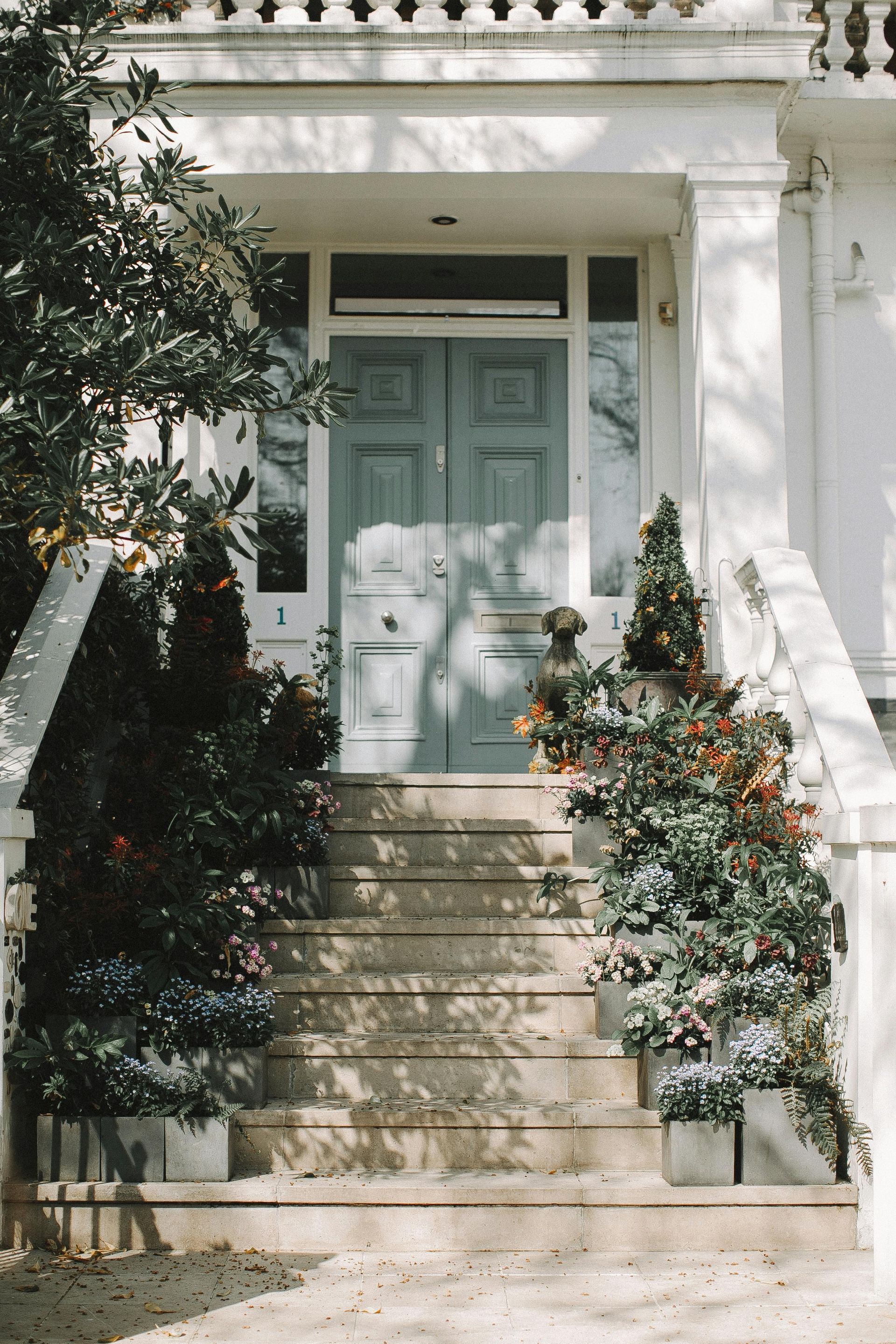 A white house with a blue door and stairs decorated with flowers.
