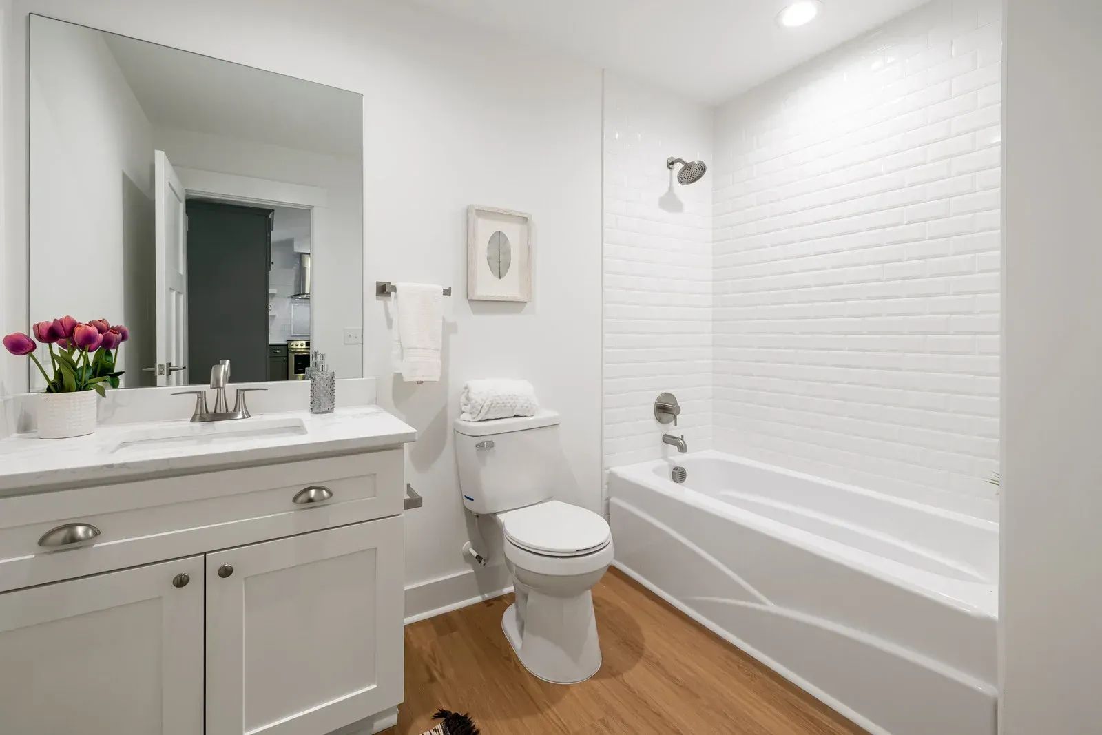 Bright white bathroom with vanity, toilet, mirror, and tub with subway tile walls