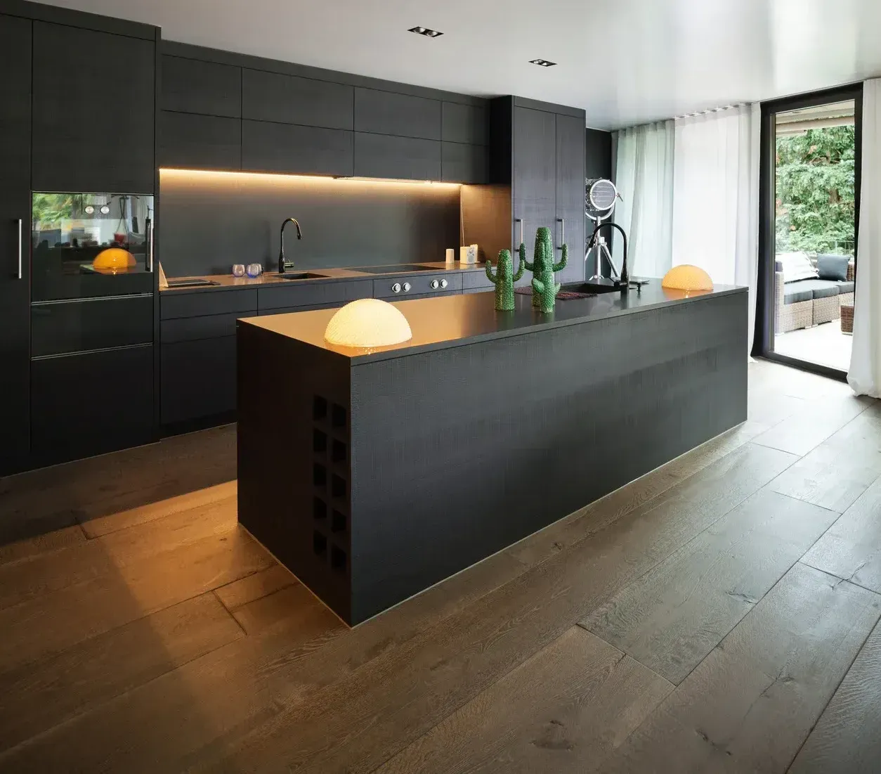 Modern black kitchen with island, wooden floors, and outdoor access.