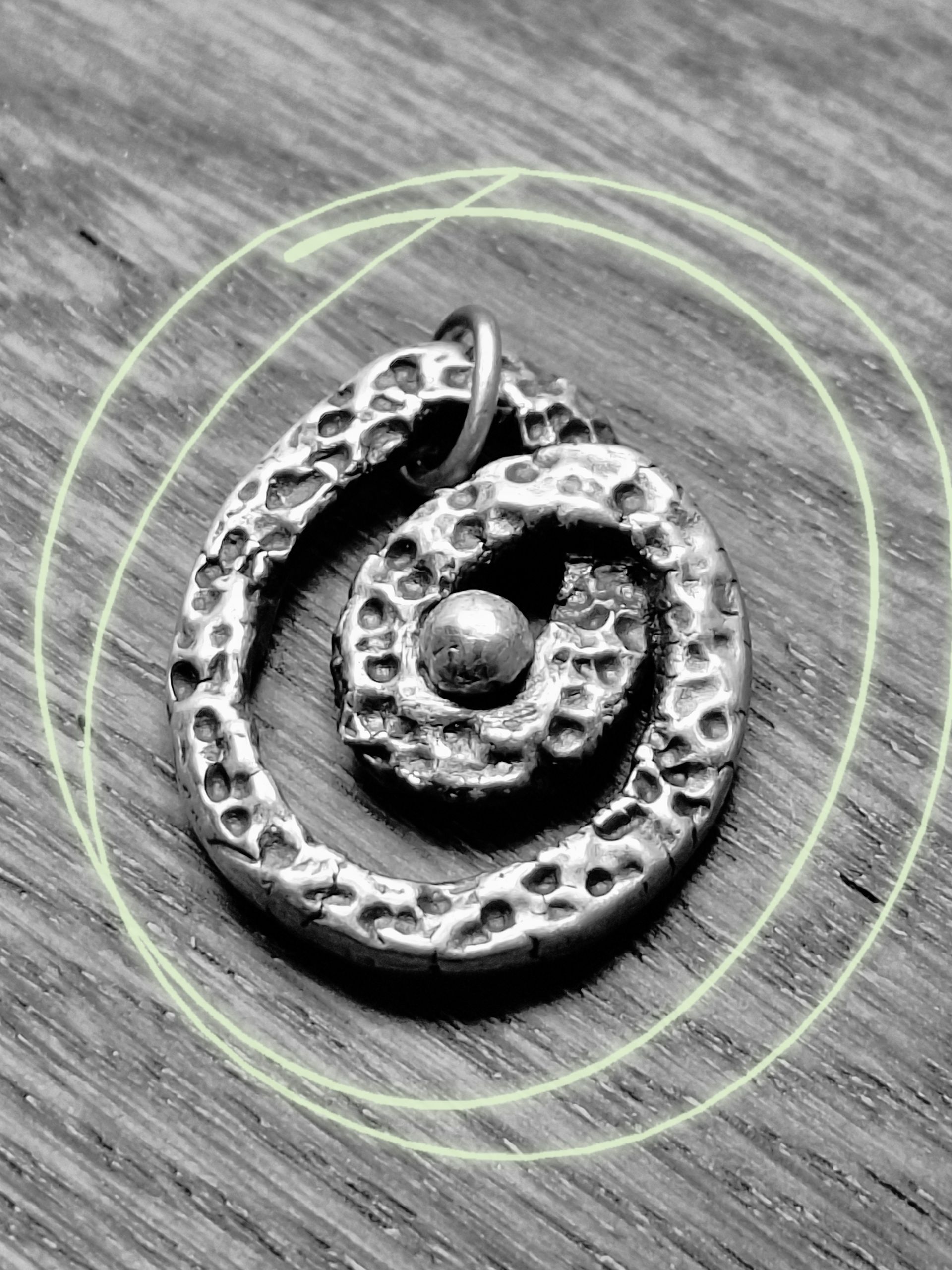 Zilveren spiraalvormige hanger met een gestructureerd oppervlak en een klein kraaltje in het midden.