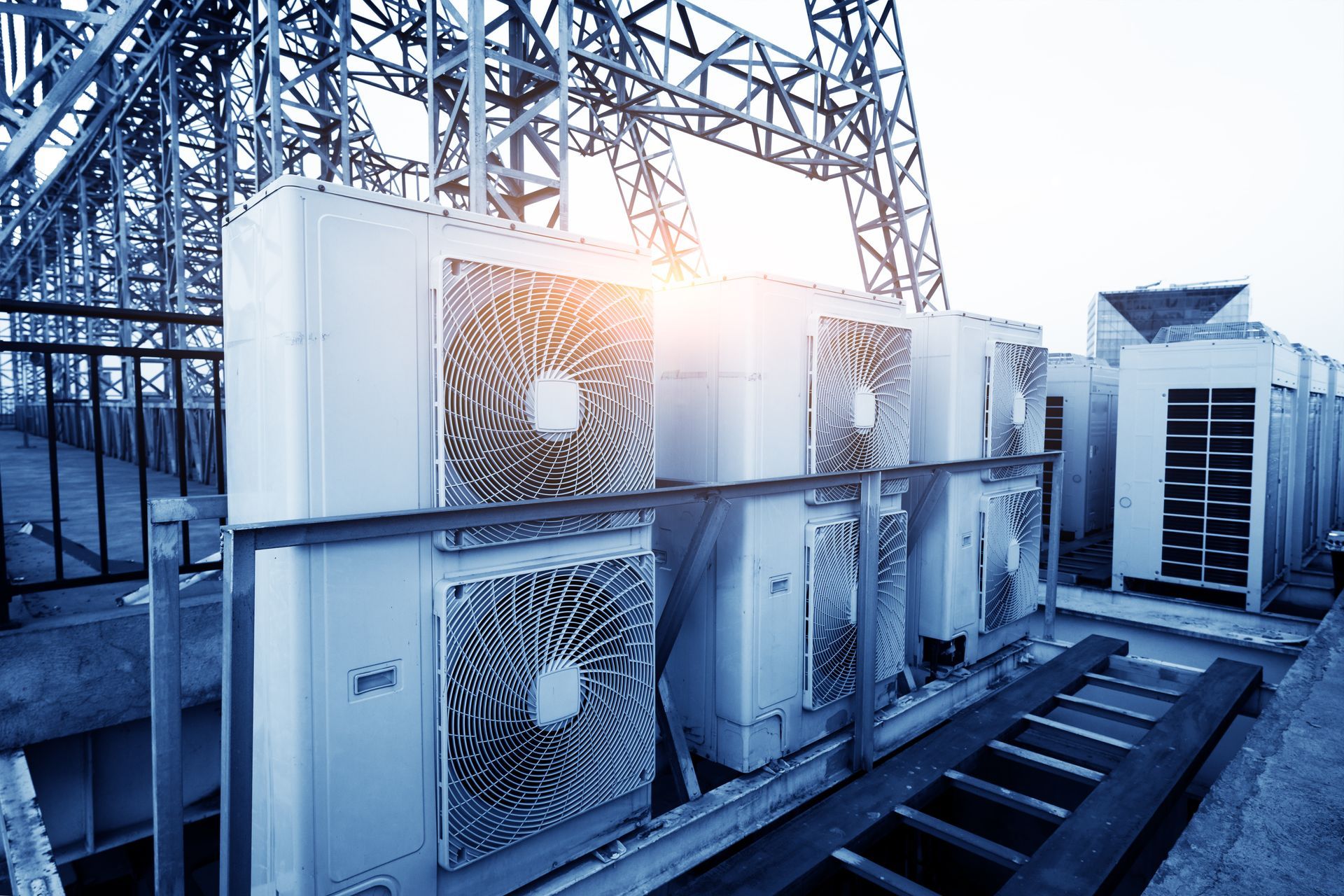 Industrial rooftop cooling units with fans and metal piping in blue daylight