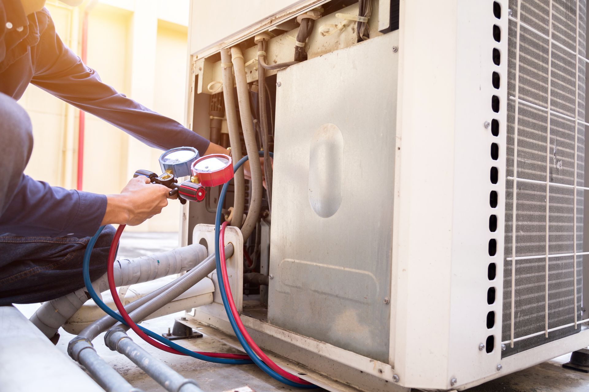 Technician using gauges to service an outdoor HVAC unit with red and blue hoses attached