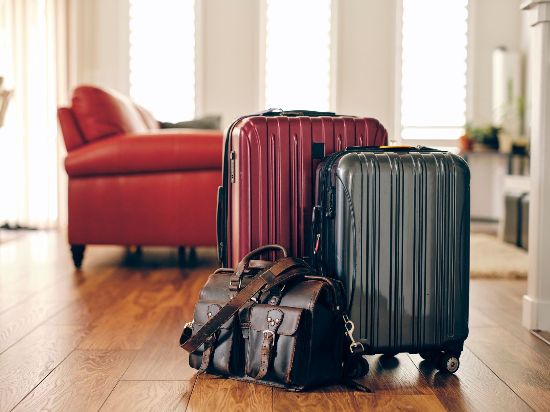Three suitcases and a bag are sitting on a wooden floor in a living room.