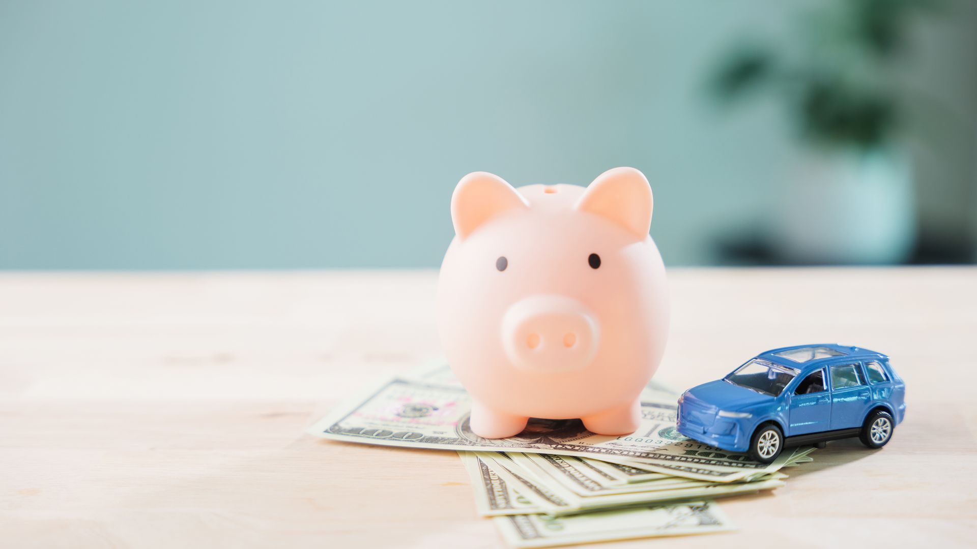 Pink piggy bank and toy car placed on cash, representing savings for vehicle expenses.