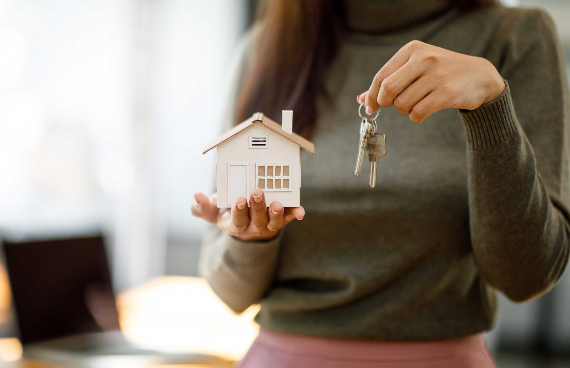 Female woman hands holding home model and keys.
