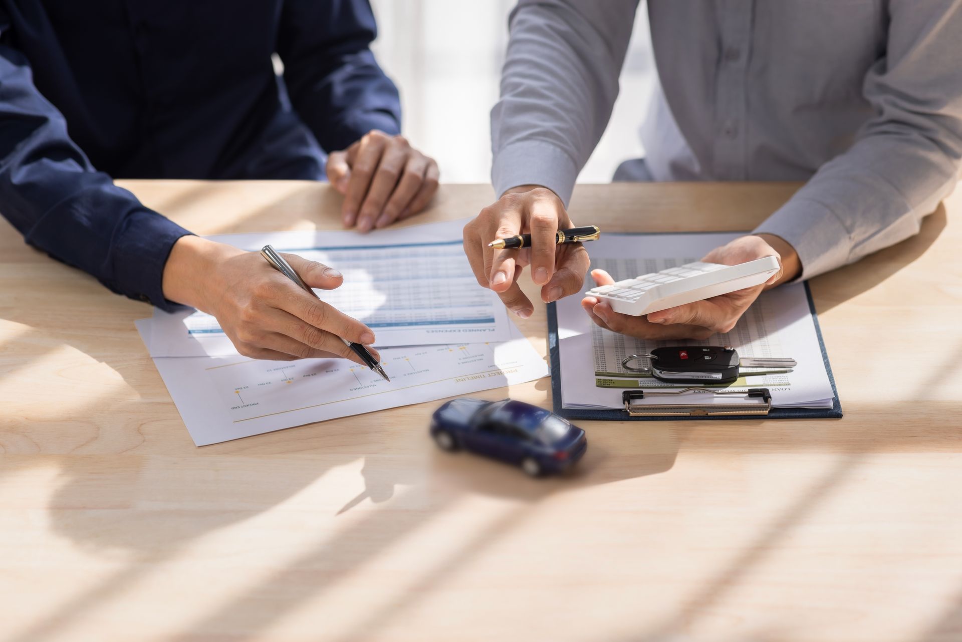 Two people are reviewing auto insurance claim documents with a calculator, pen, and clipboard
