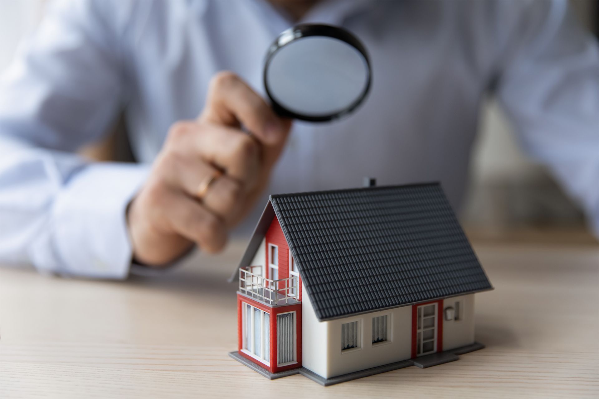 man examining a miniature house with magnifying glass