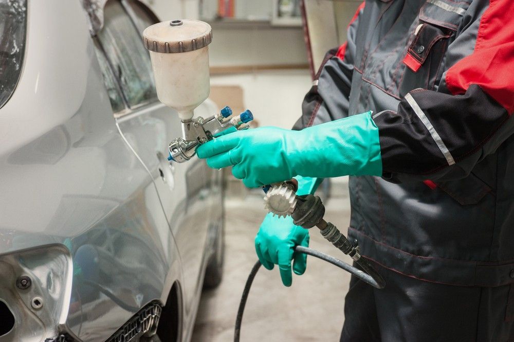 A Man Wearing Green Gloves is Spraying Paint on a Car — Dawson Crash Repair In Aitkenvale, QLD