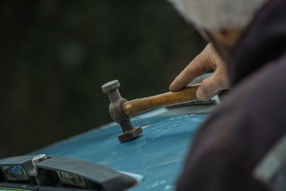 A Person is Holding a Hammer on Top of a Blue Car — Dawson Crash Repair In Aitkenvale, QLD