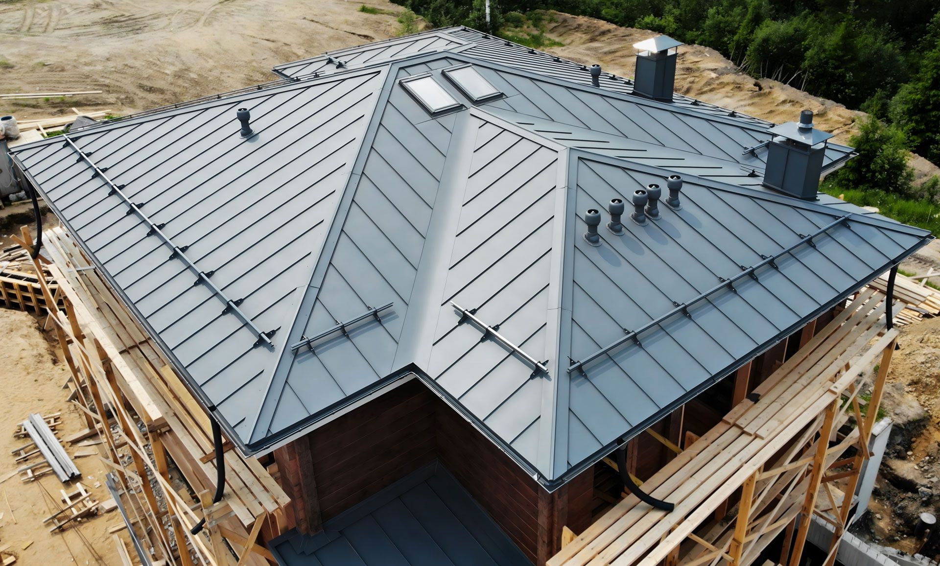 Gray metal roof on a house under construction, with skylights and chimneys.