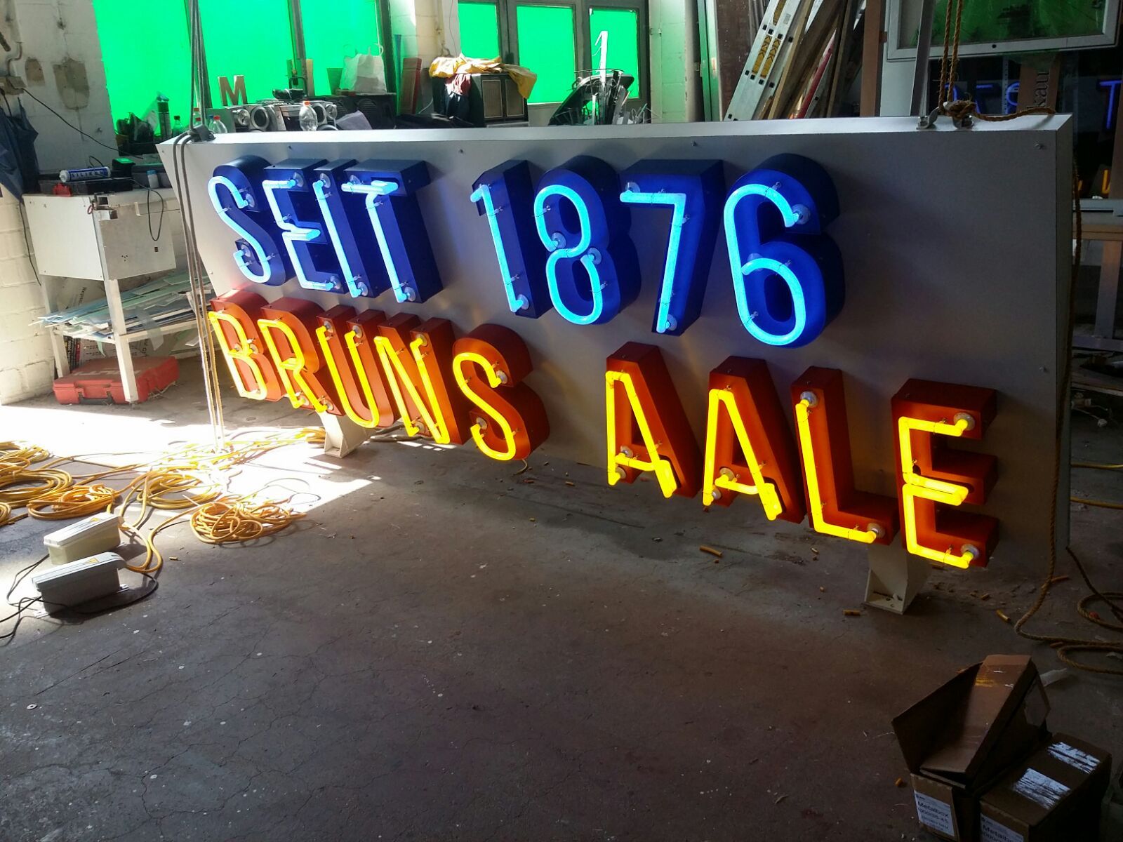 Leuchtreklame „SEIT 1876 BRUNS AALE“ in blau/orange, teilweise beleuchtet, in Werkstatt-Umgebung.