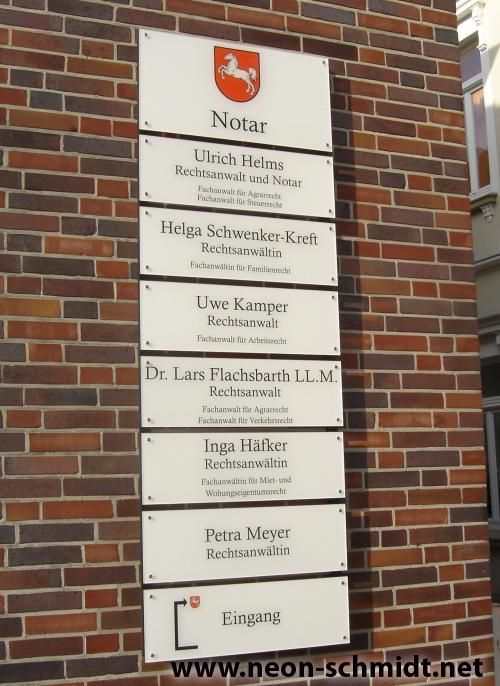 Schild mit Namen von Notaren und Anwälten an einer Ziegelmauer, mit Eingangsbeschriftung.