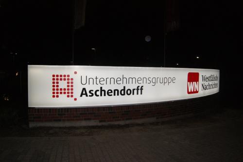 Leuchtreklame der Unternehmensgruppe Aschendorff bei Nacht. Weiß mit roter und dunkler Schrift.