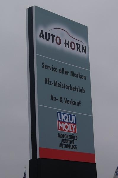 Schild für „Auto Horn“ mit Servicedetails und Liqui Moly-Logo. Grau und Schwarz, Außenbereich.
