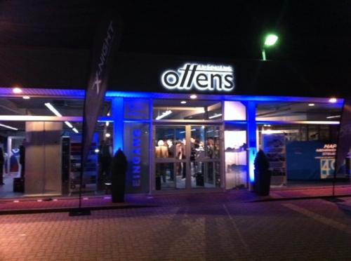 Außenaufnahme eines Ladens bei Nacht mit hellblauem Licht. Auf dem Schild steht „Offens“.